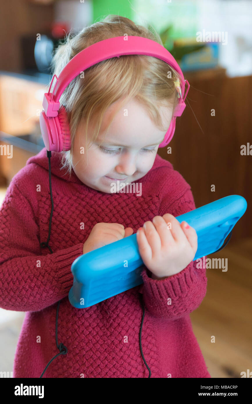 A toddler wearing headphones and using an electronic tablet. Stock Photo