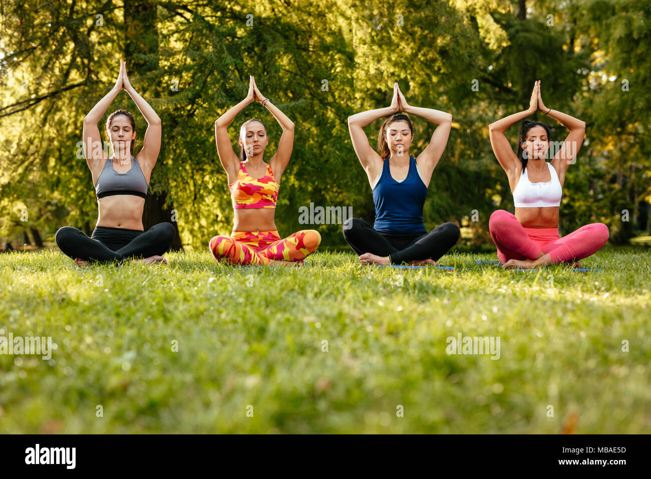 Fitness group of four young women doing yoga meditation in the city park. Stock Photo