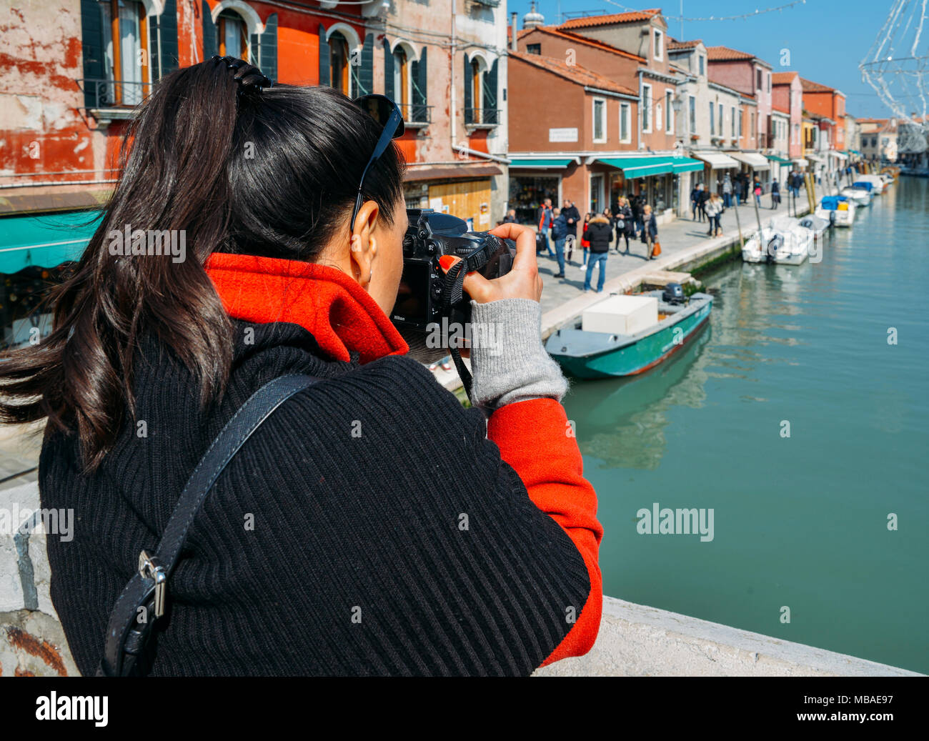 Young brunette woman takes a picture of a colorful canal in Murano with a DSLR camera Stock Photo