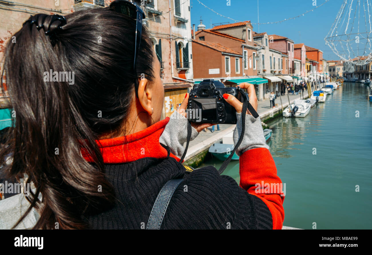 Young brunette woman takes a picture of a colorful canal in Murano with a DSLR camera Stock Photo