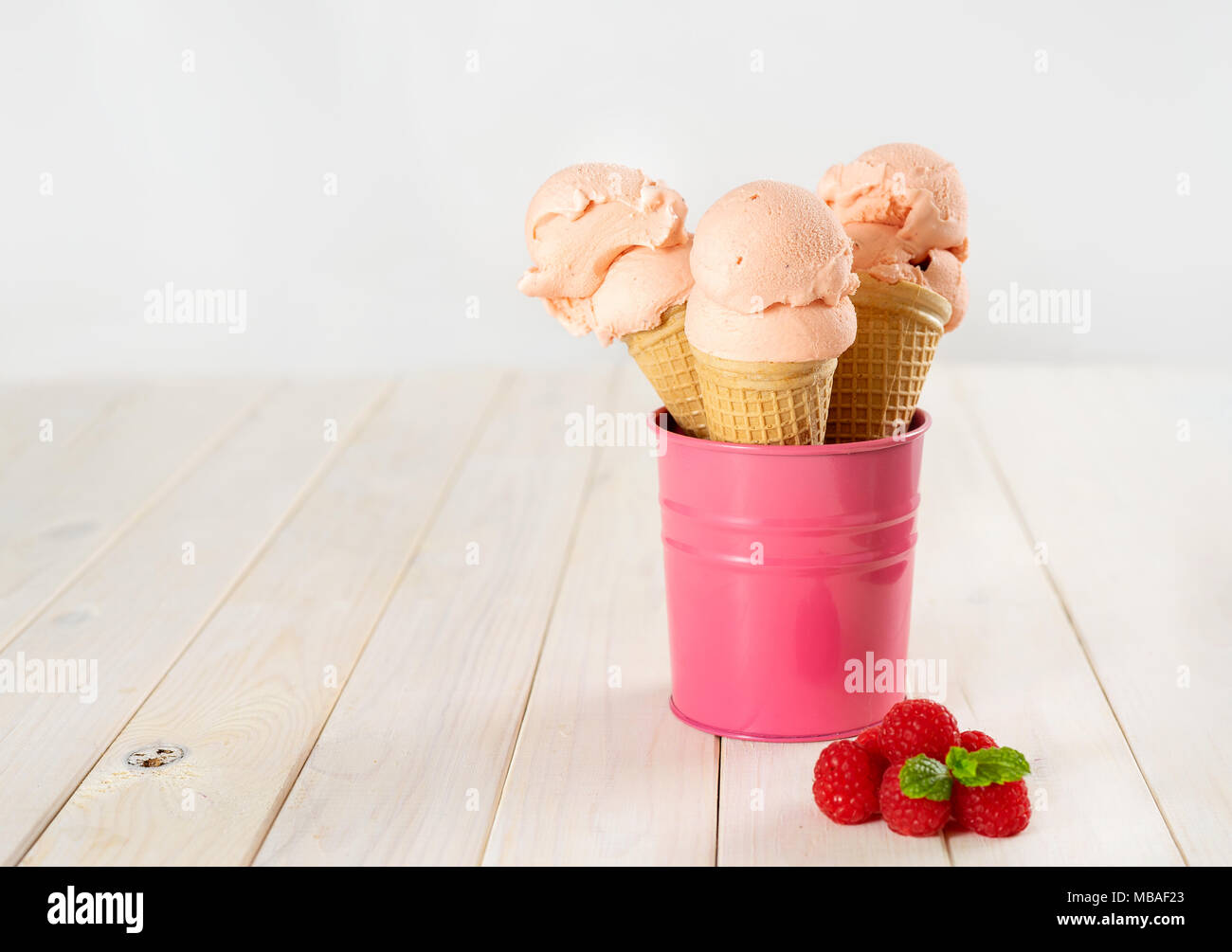 Three raspberry ice cream cones places in pink bucket in white wooden table Stock Photo Alamy