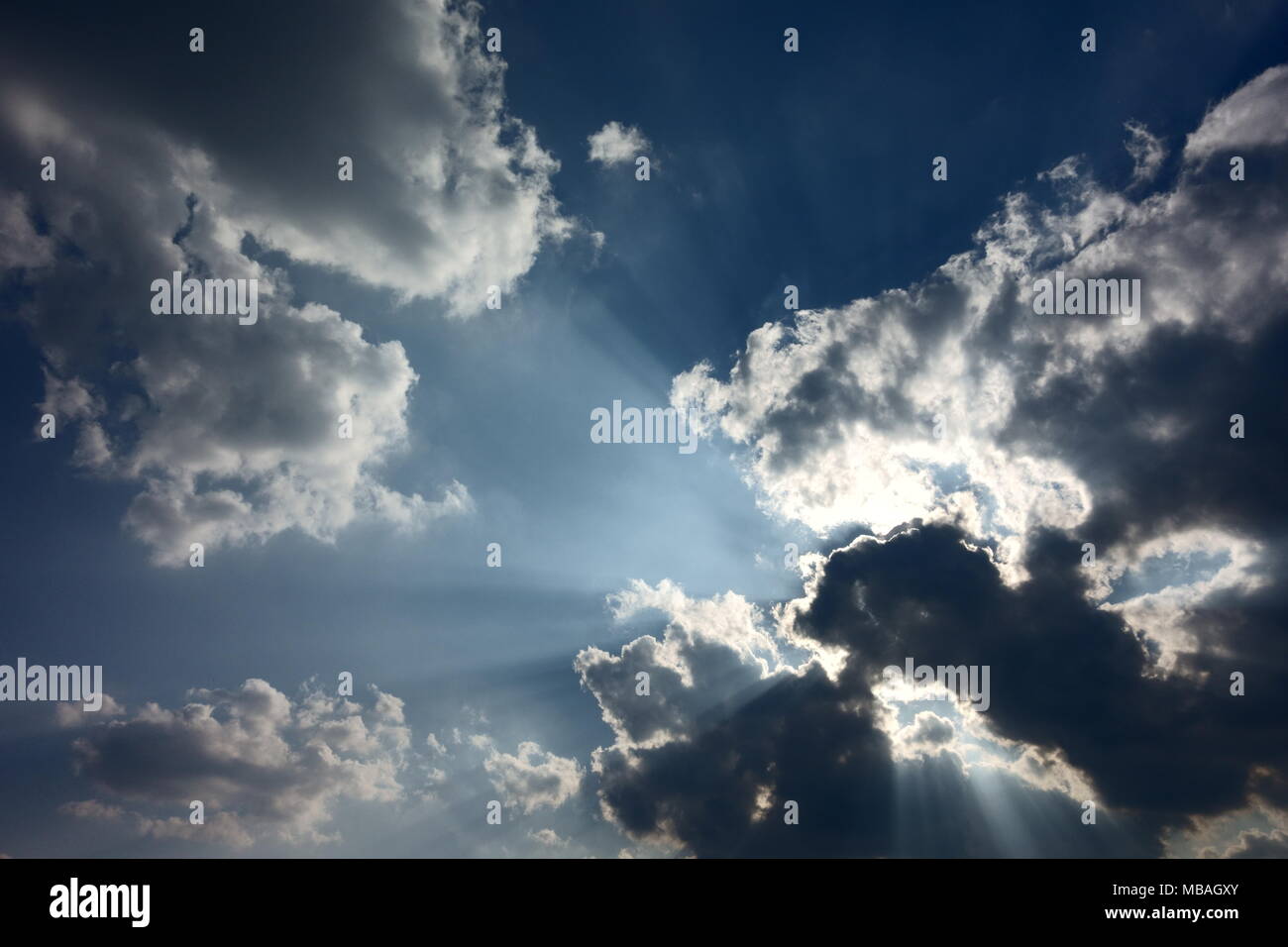 Blue skies with some cumuli obscuring the sun; rays of light, silver linings Stock Photo