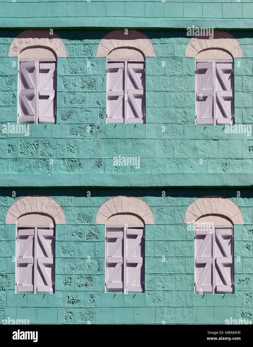 detail of two-story green warehouse made with coral blocks with shuttered arched windows. Stock Photo