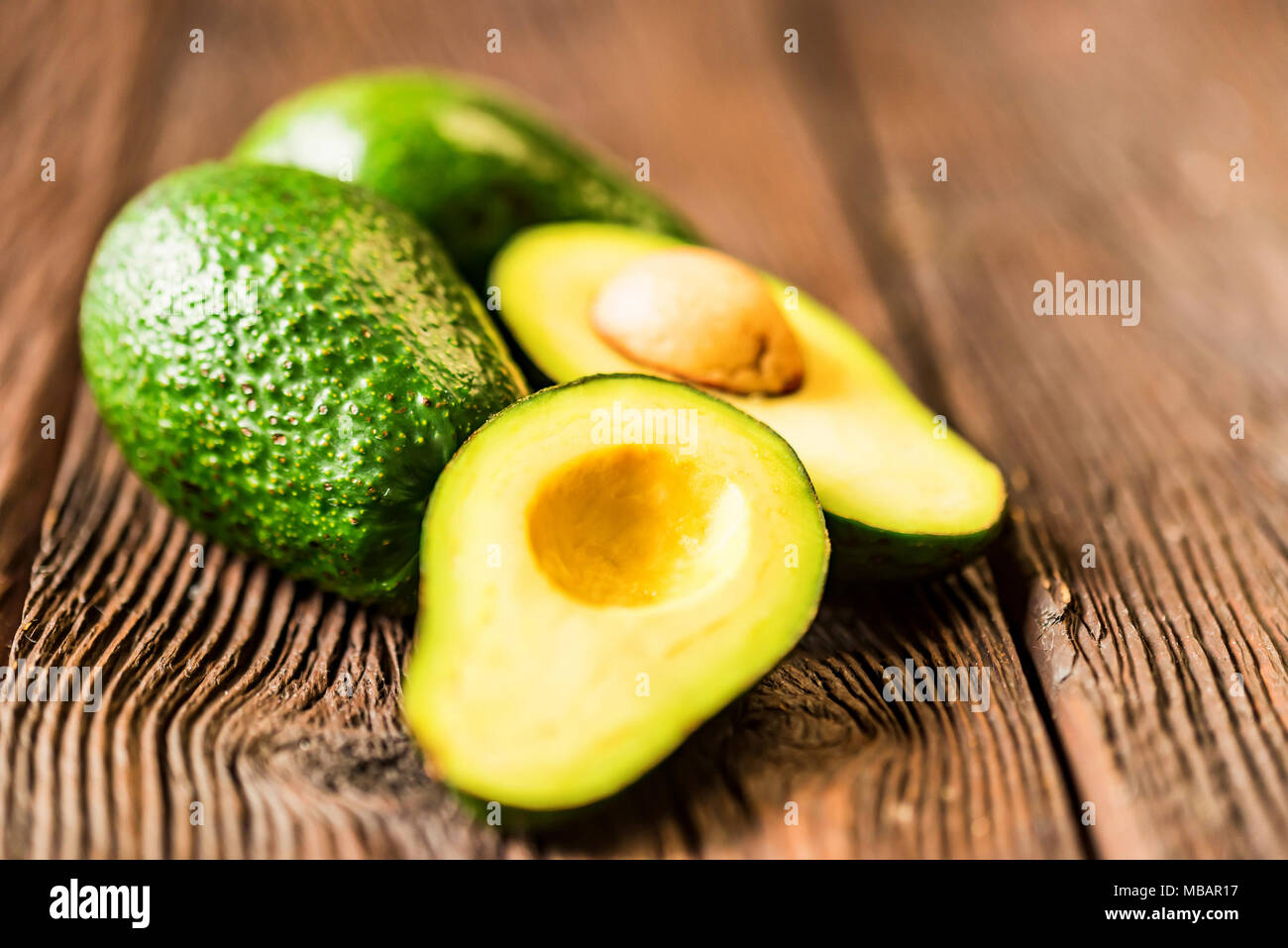 Avocados cut and whole on a wooden background Stock Photo - Alamy