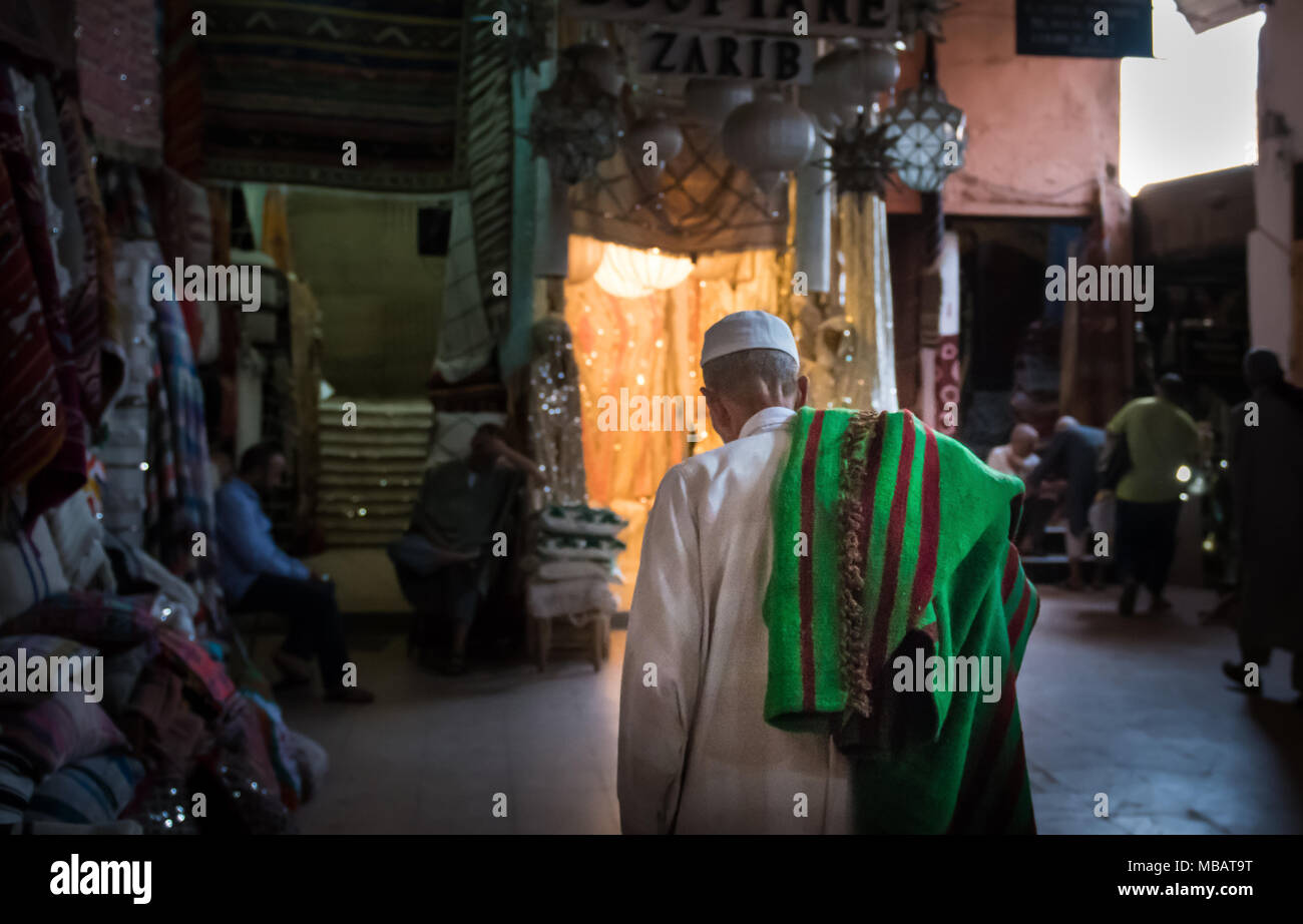 A moroccan man walks with a green and red carpet slung over his shoulder in the Marrakech carpet market in Morocco. Stock Photo
