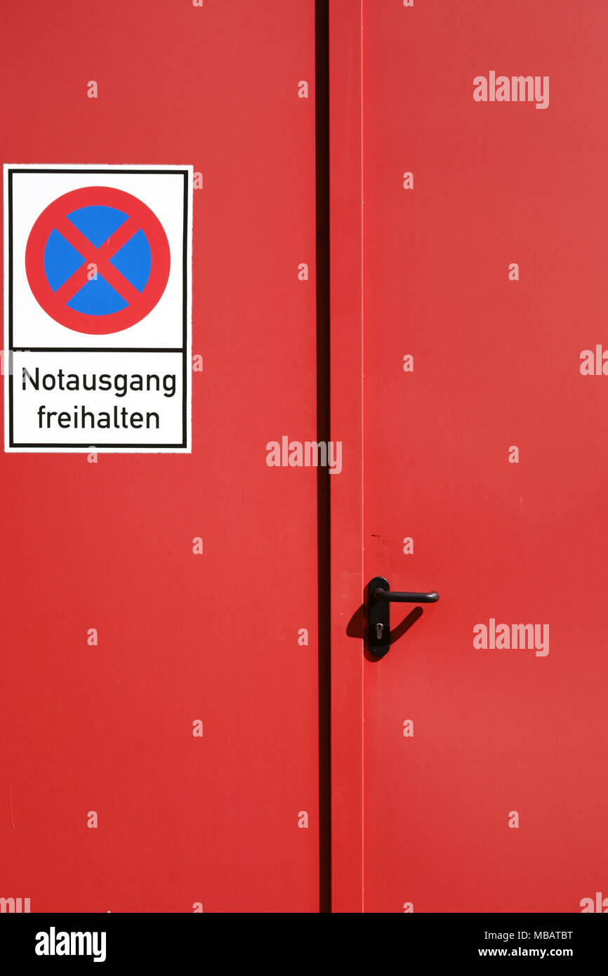A bright red painted emergency exit from a steel door with a sign. Stock Photo