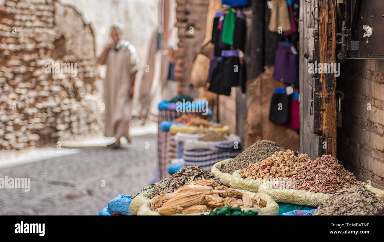 Piles of Spices and herbs in tall baskets in front of a spice shop in Marrakech, Morocco. A Moroccan man in the djellaba is walking in the background. Stock Photo