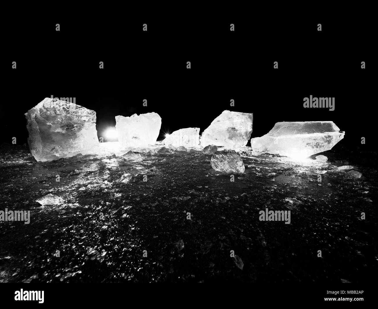 Blue ice cubes shine on flat glacier surface. Thanks to spot light