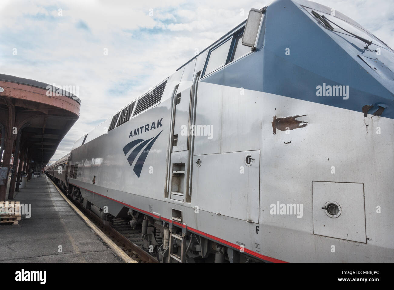 Engine showing slight damage, Amtrak train idles at station platform