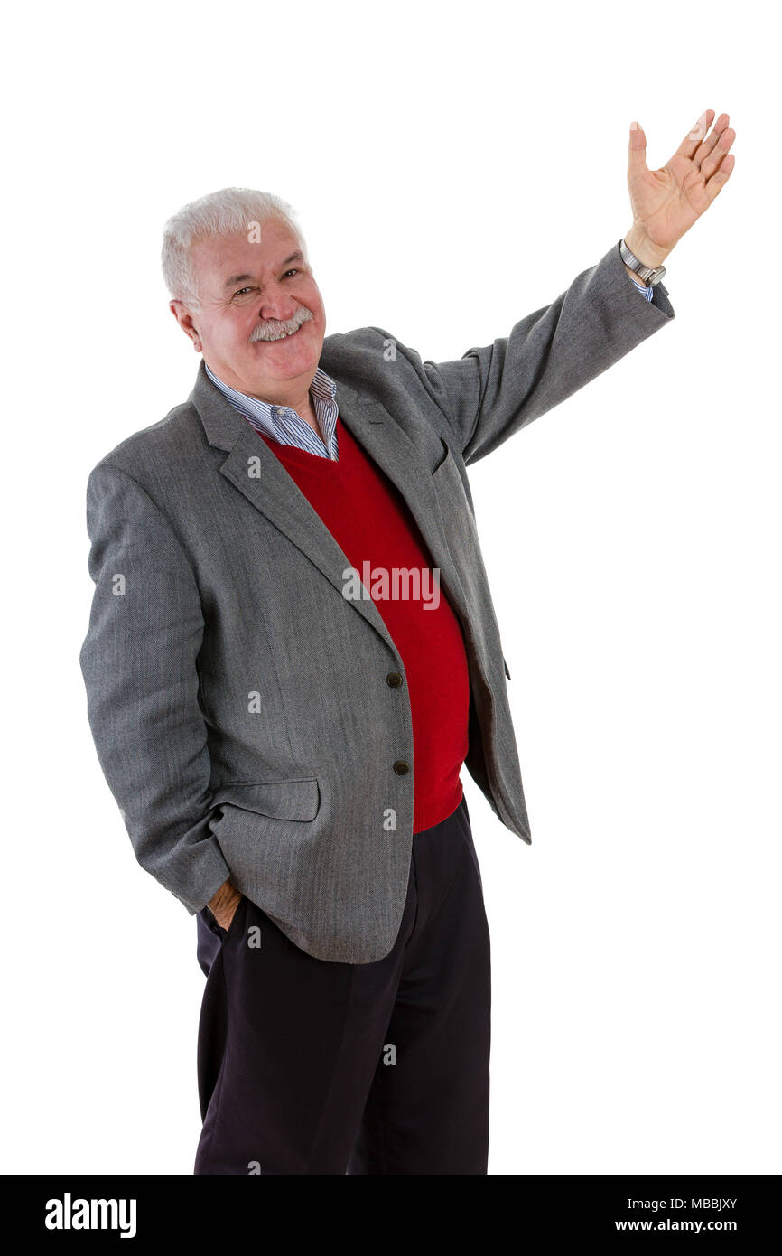 Smiling relaxed happy senior man with raised arm and other hand in his pocket turning to smile at the camera as he draws your attention to something i Stock Photo