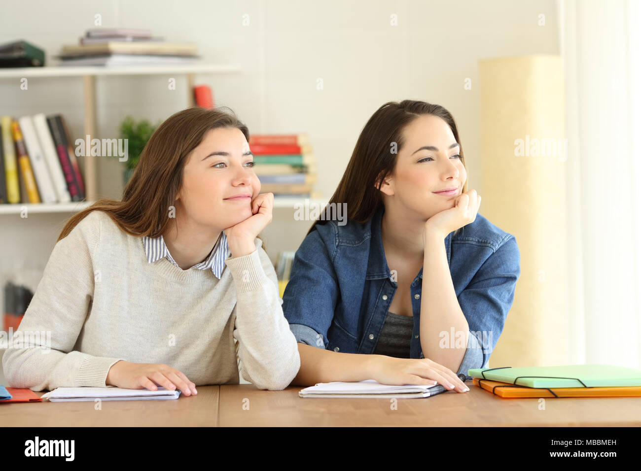 Two candid students dreaming looking at side through a window at home Stock Photo