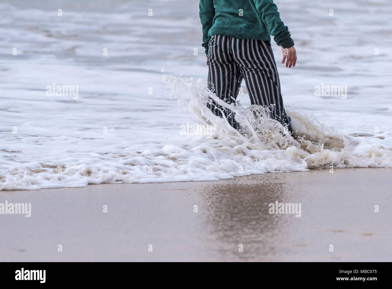 A person standing in the sea as waves break around her legs. Stock Photo