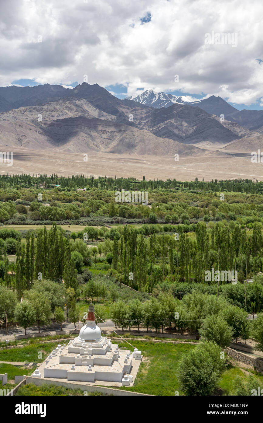 White stupa near Shey Monastery; trees and vegetation of Indus river valley floodplain; arid mountains of Stok range and highest of all Stok Kangri Stock Photo