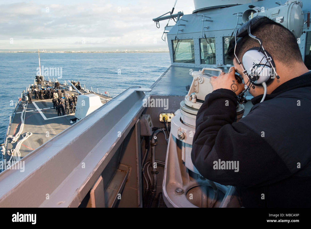 PEARL HARBOR (Feb. 16, 2018) Operations Specialist 2nd Class David Artellano, from Chicago, assigned to Arleigh Burke-class guided-missile destroyer USS Dewey (DDG 105), looks through a telescopic alidade on the ship's port bridge wing as the ship pulls into Pearl Harbor for a port visit. Dewey is on a scheduled deployment to conduct operations in the Indo-Pacific region.  It will also support the Wasp Expeditionary Strike Group (ESG) in order to advance U.S. Pacific Fleet's Up-Gunned ESG concept and will train with forward-deployed amphibious ships across all mission areas. (U.S. Navy Stock Photo