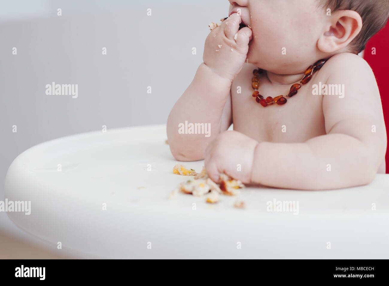 Close crop of 6 month old baby boy feeding himself in a high chair Stock Photo