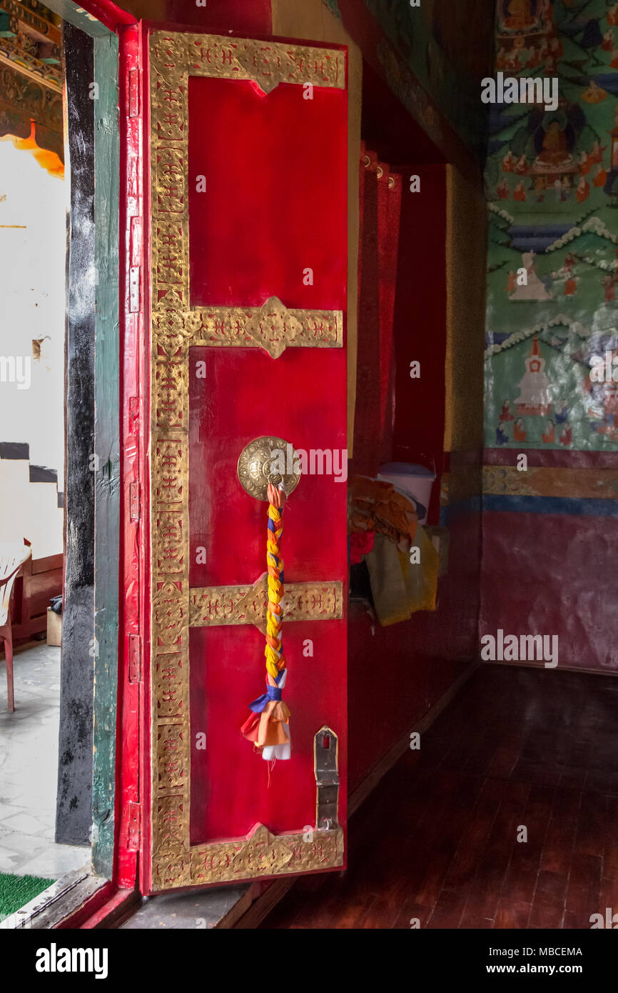 Sturdy temple door painted bright scarlet and adorned with golden trim, and a brass door knocker with a plait of colourful wool. Stock Photo