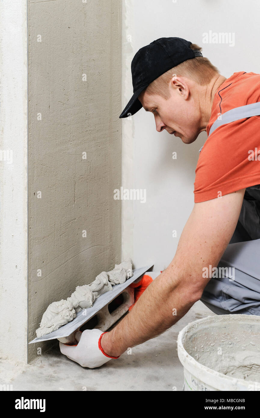 The worker puts f inishing layer of stucco on the wall using a