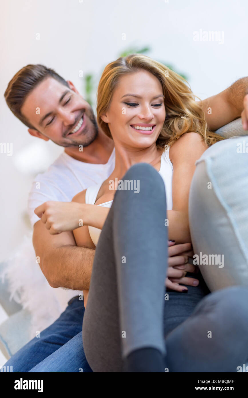 A beautiful young woman lying on the sofa with boyfriend hugging her ...