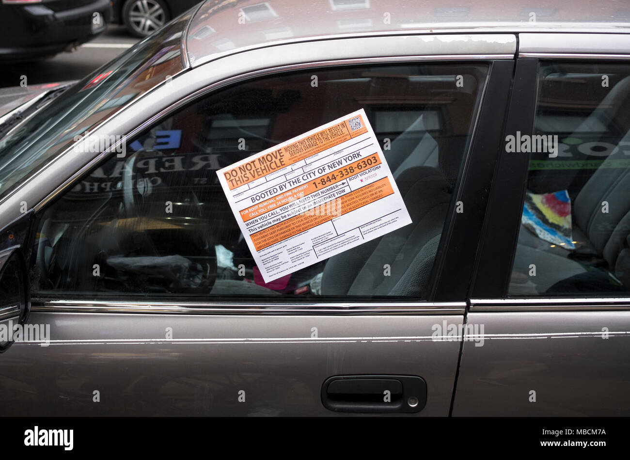 A notice on a parked car in Cobble Hill, Brooklyn that has been booted by the City for parking violation or violations. Stock Photo