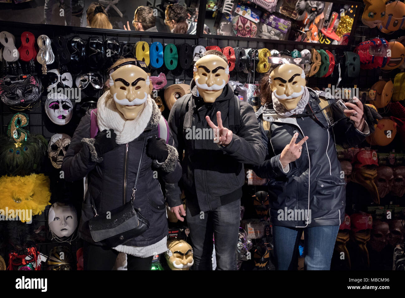 3 French tourists pose for a photo in the mask section of the Halloween Adventure costume store on Broadway in Greenwich Village. Stock Photo