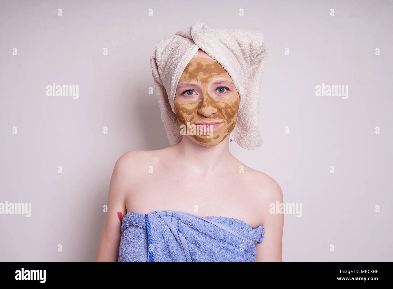 young woman with healing earth or clay beauty facial mask wrapped in towel Stock Photo