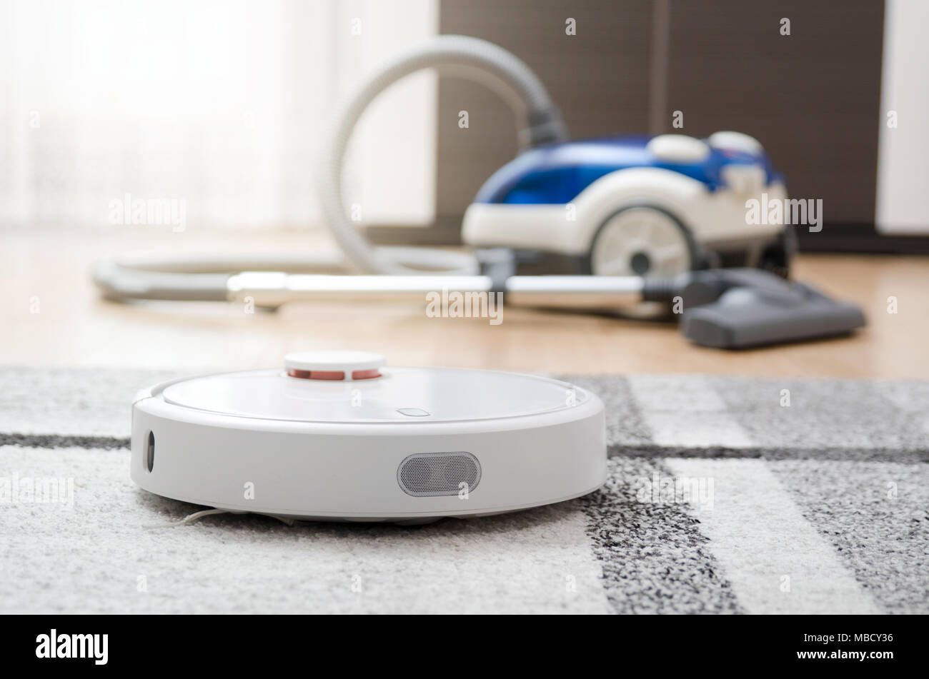 Robotic vacuum cleaner cleaning the room. Classic vacuum cleaner in the background Stock Photo