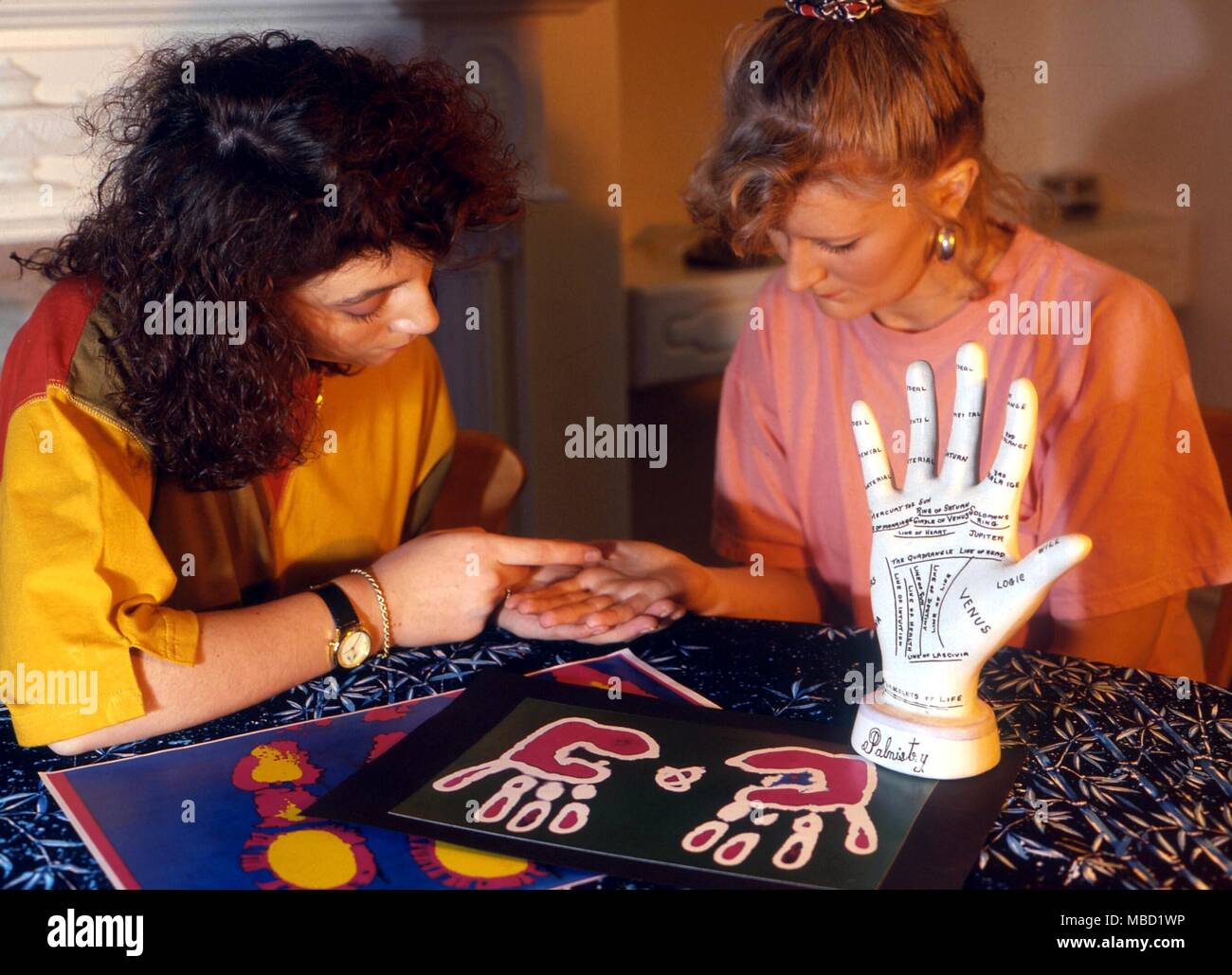 Palmistry Girl reading the hand of another girl, with a palm-print analyses, and a Victorian ceramic palmist hand. Stock Photo