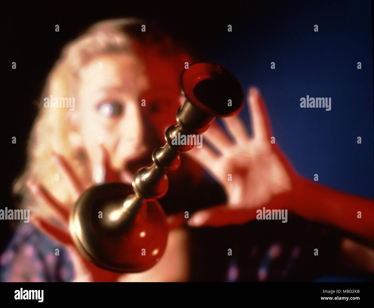 Woman trying to avoid a heavy candlestick thrown by a poltergeist. Stock Photo