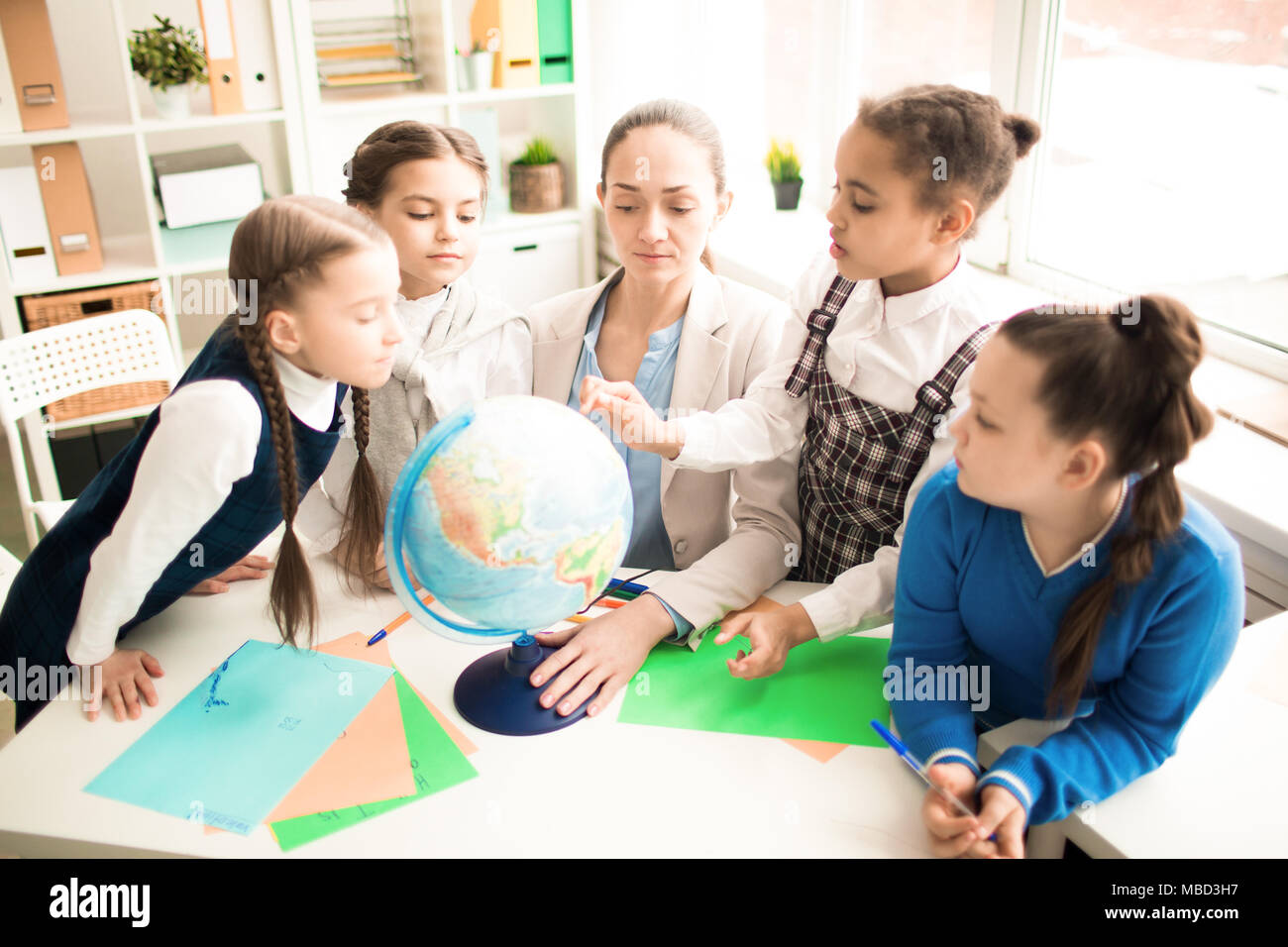 Cute pupils and teacher in classroom with globe at the primary school ...
