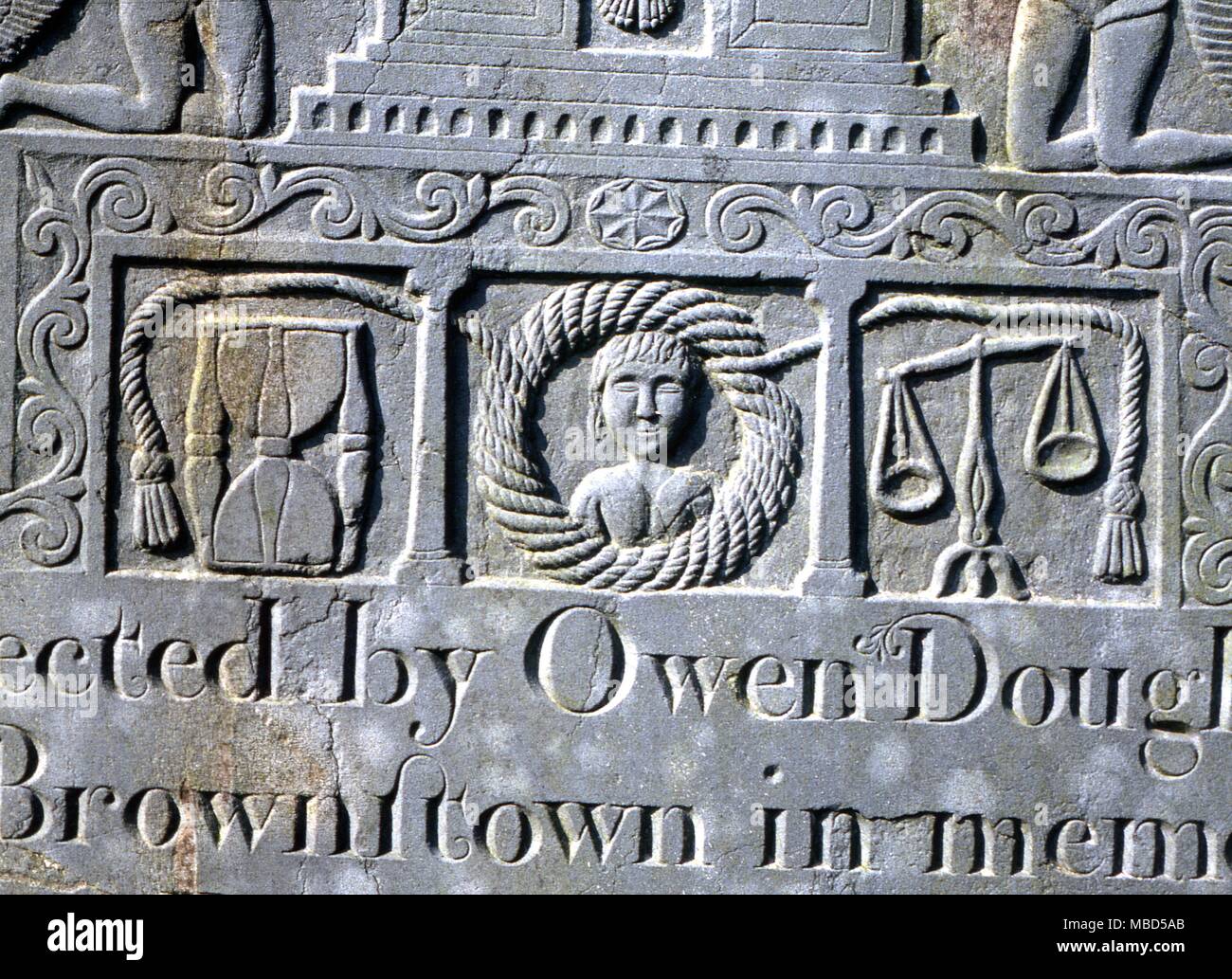 Symbols - Hour Glass. Headstone of the early 19th century, with bas relief of Crucifixion and various symbols of death and resurrection, including hour glass and scales. Ireland. Stock Photo