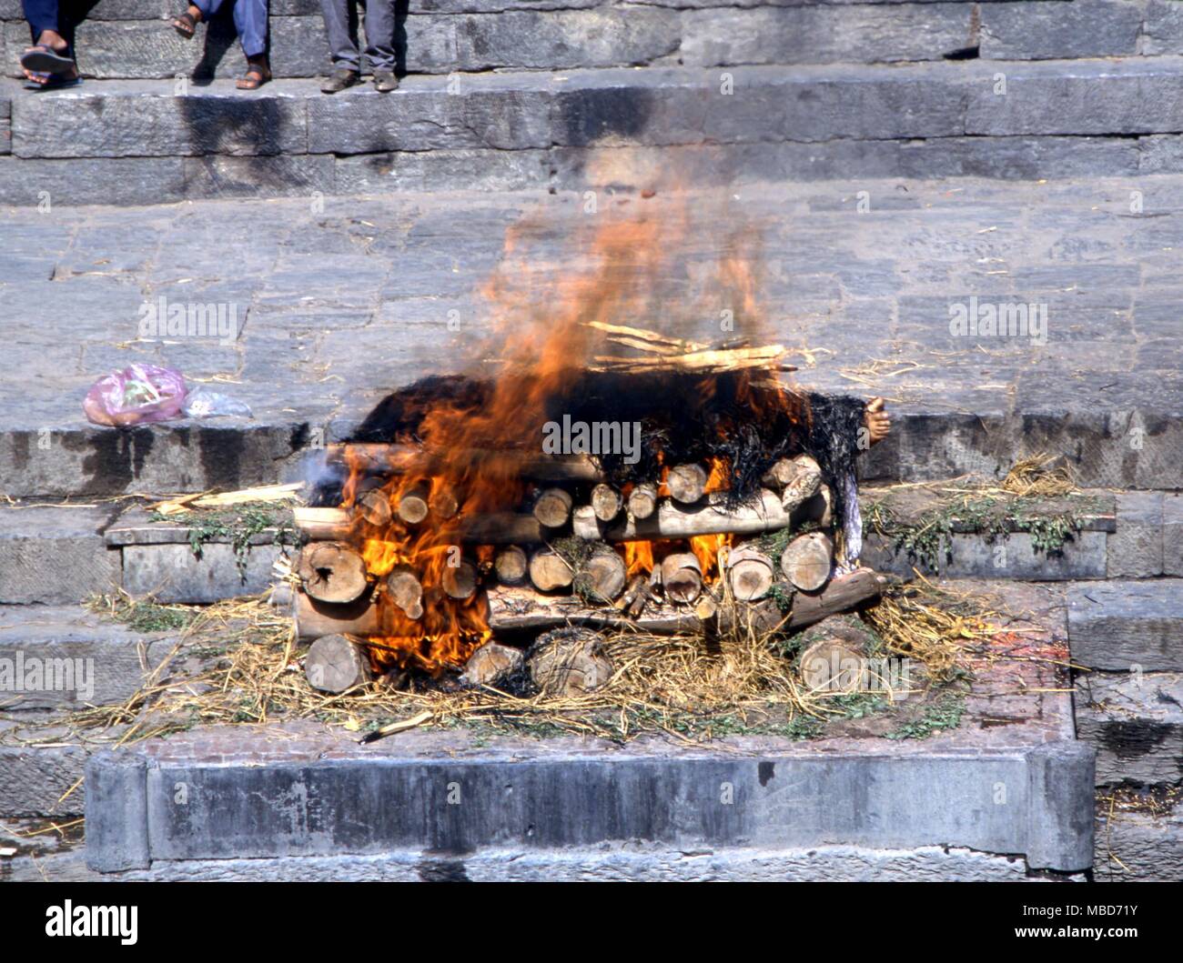 Death - Hindu cremation - Cremation of a dead body by the Bagmati River (Kathmandu valley). The corpse, removed of its clothing beneath the straw, is burned. The ashes are then thrown into the river. Stock Photo