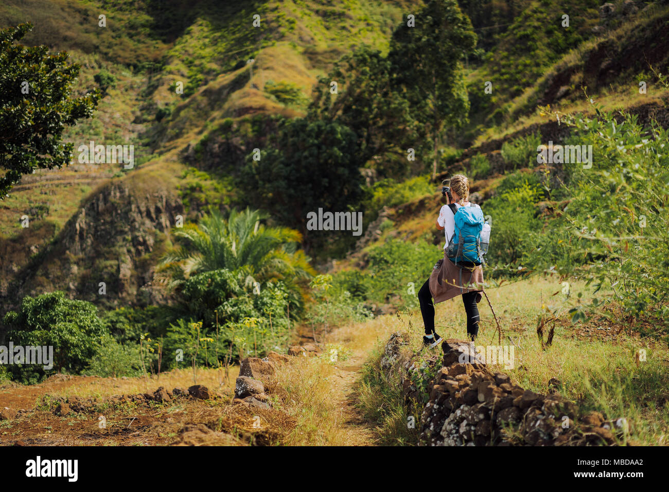 Woman tourist with blue backpack making photo of landscape in Mountains of Santo Antao island, Cabo Verde Stock Photo