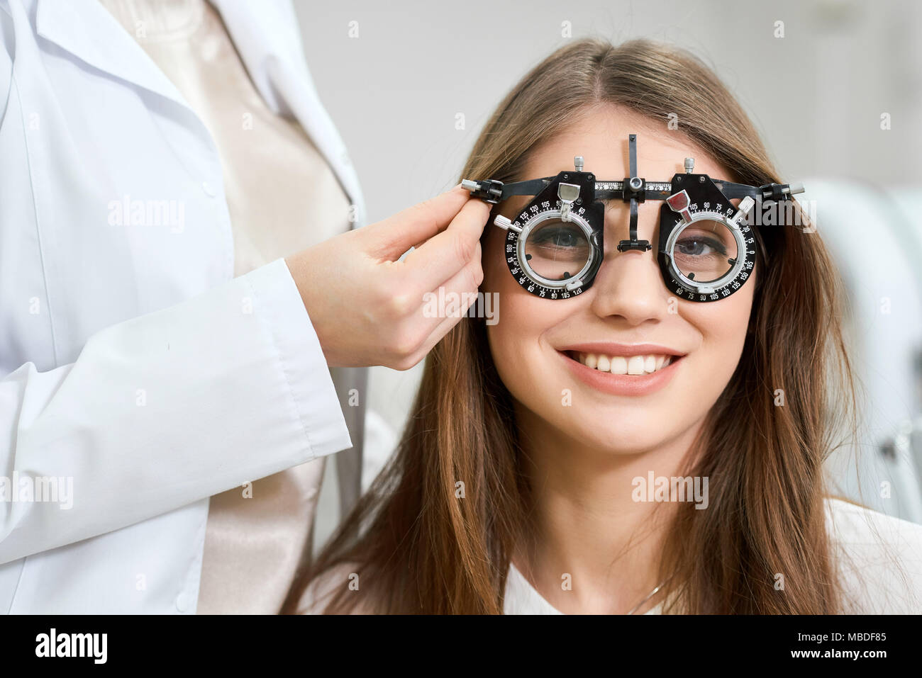Young pretty patient wearing visual inspection device during admission to an ophthalmologist. Health saving, vision imroving. Feeling satisfied. Doctor is giving advices. Stock Photo