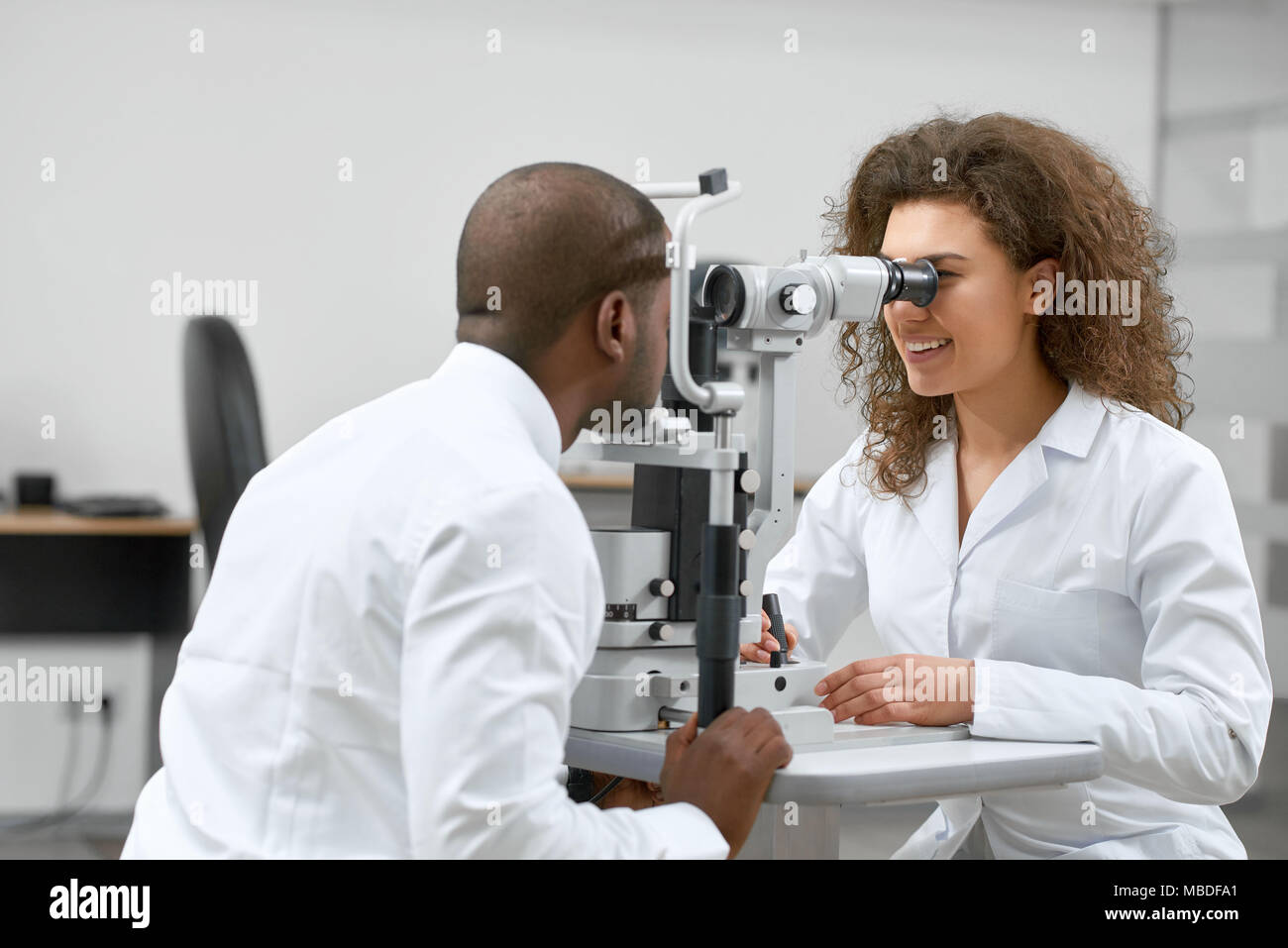 Photo of patient looking at medical apparatus during vision checking in ophthalmological laboratory with expirienced ophthalmologist..Trying to improve vision in modern oculist' cabinet. Stock Photo
