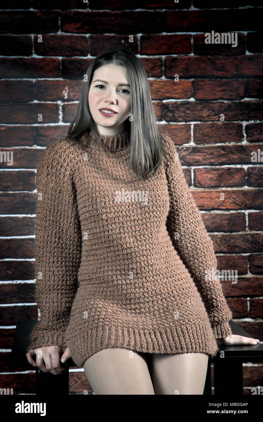 girl in sweater leans on coffee table on brick wall background Stock Photo