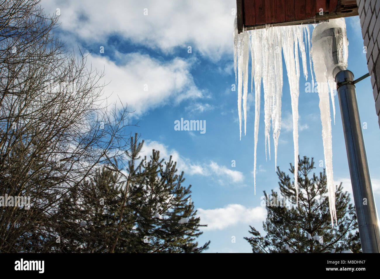 Large icicles hang from the roof of the house against the sky Stock Photo