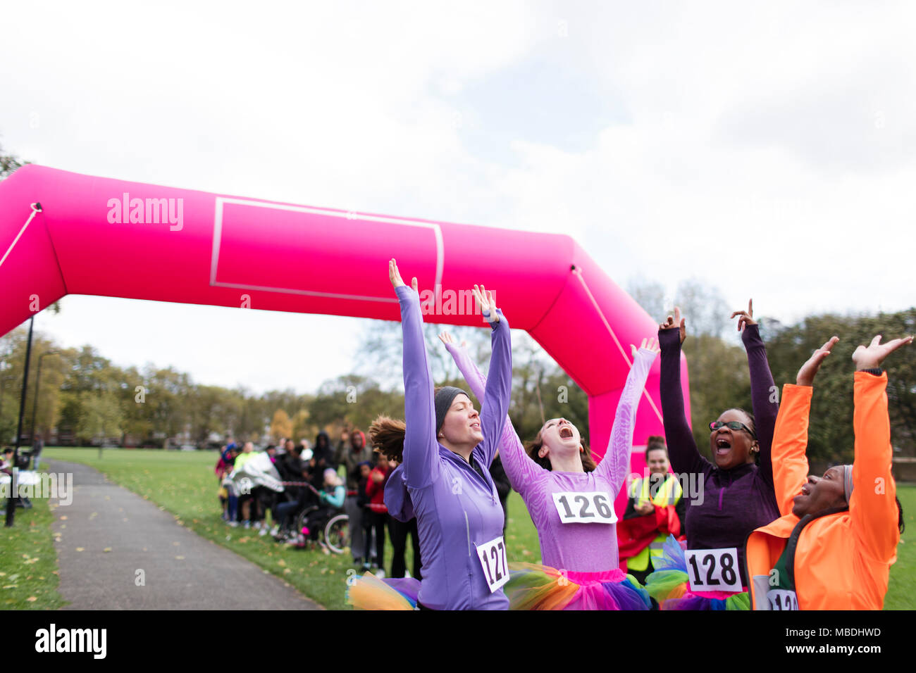 Enthusiastic female runners in tutus cheering, celebrating at charity run finish line Stock Photo