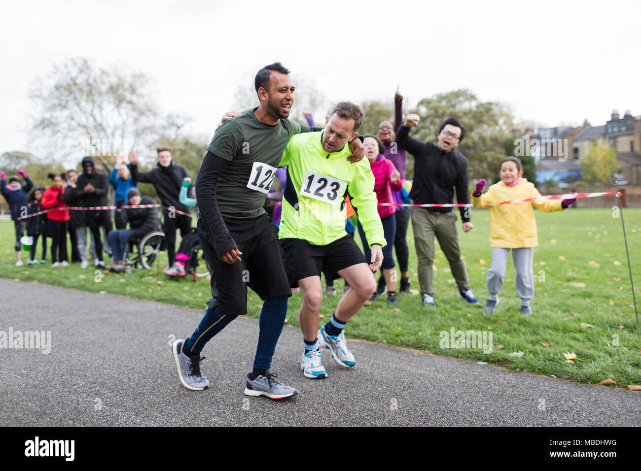 Spectators cheering for man helping injured marathon runner Stock Photo