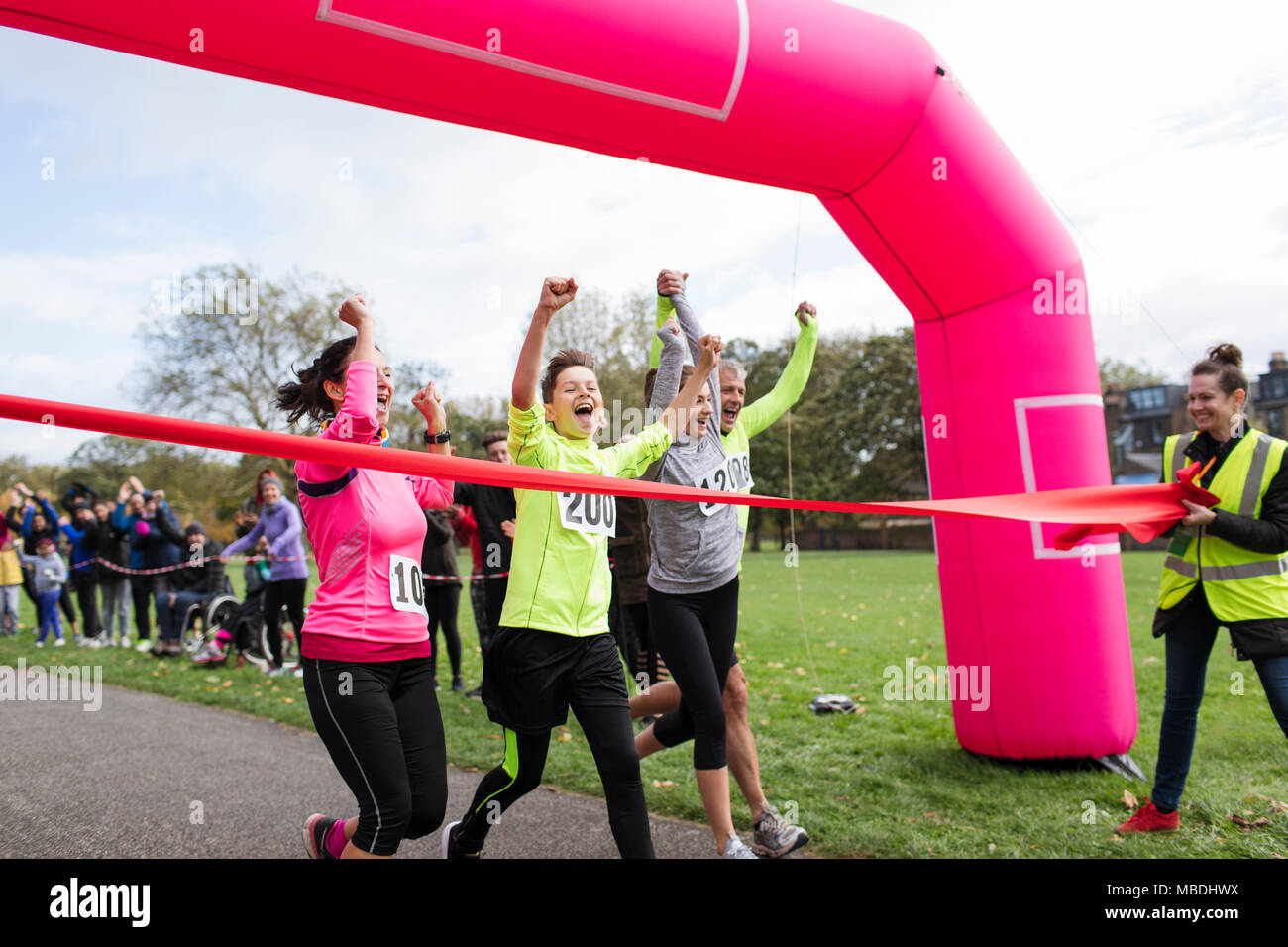 Enthusiastic family runners crossing charity run finish line in park Stock Photo