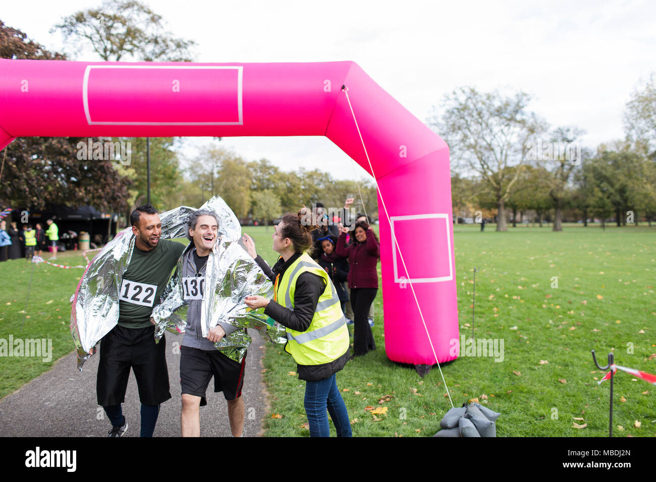 Volunteer wrapping male runners in thermal blanket at marathon finish