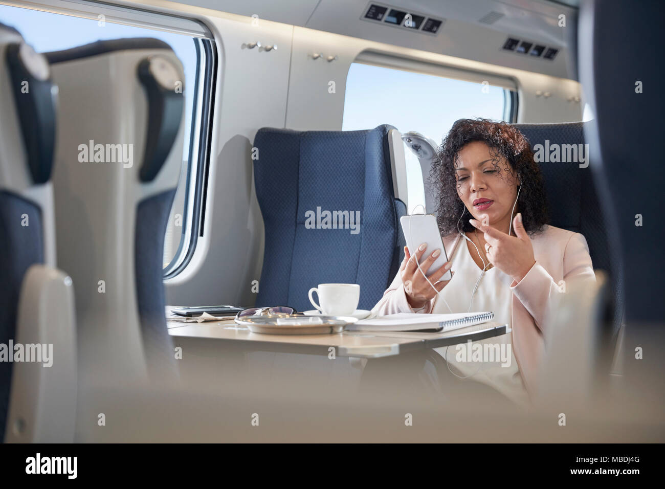 Businesswoman video chatting with headphones and smart phone on passenger train Stock Photo