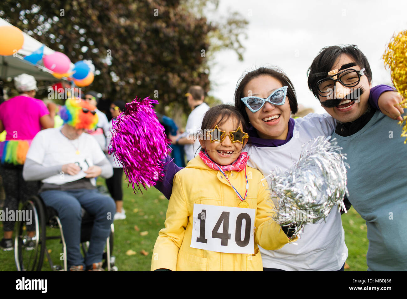Portrait playful family wearing silly eyeglasses at charity run in park Stock Photo