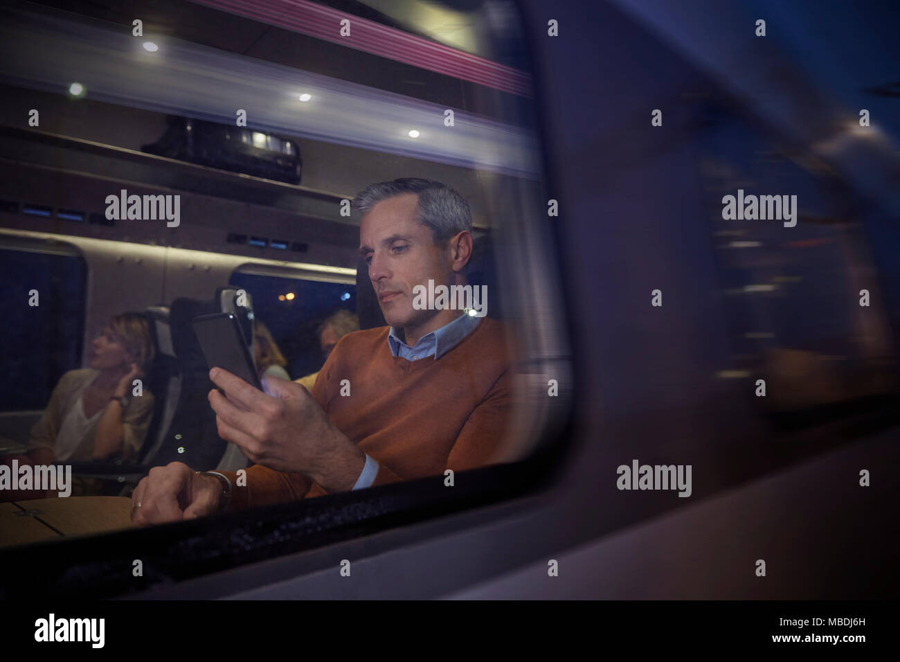 Businessman using smart phone at window on passenger train at night Stock Photo