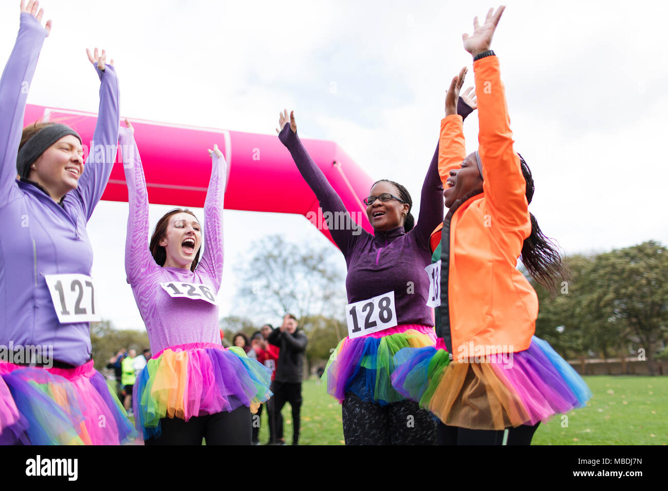 Enthusiastic female runners in tutus cheering, celebrating at charity run finish line Stock Photo