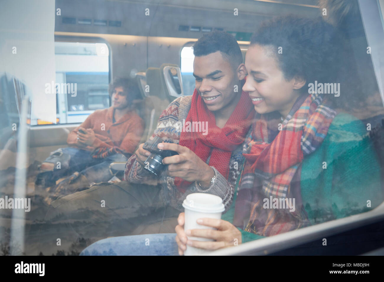 Young couple with coffee looking at digital camera at window on passenger train Stock Photo