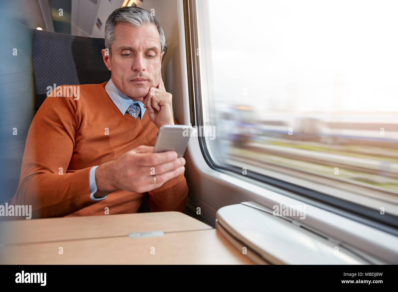 Focused businessman using smart phone at passenger train window Stock Photo