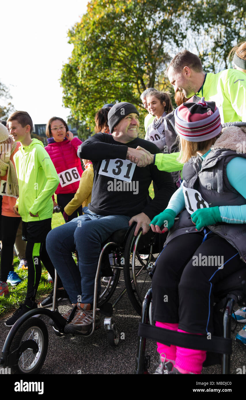 Man in wheelchair shaking hands with runner in crowd at charity race Stock Photo