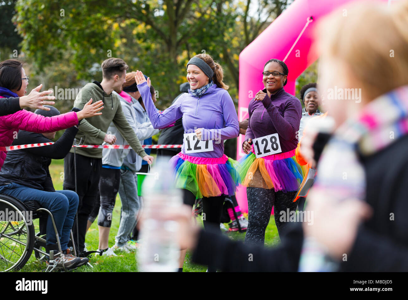 Female runners high-fiving spectators at charity run finish line Stock Photo