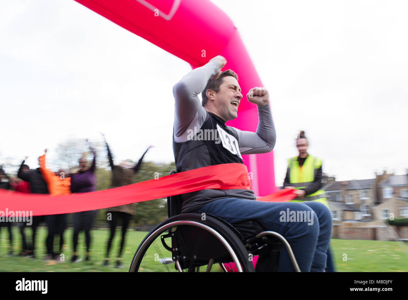 Enthusiastic man in wheelchair crossing finish line, cheering at charity race in park Stock Photo