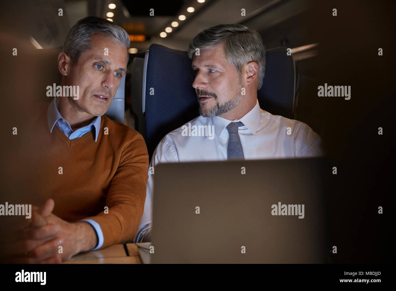 Businessmen talking, working at laptop on passenger train at night Stock Photo